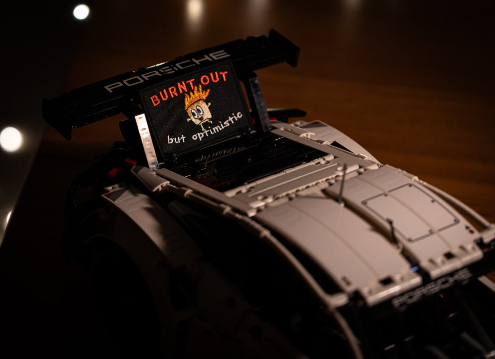 'Burnt Out but Optimistic' patch on a Lego Porsche car 