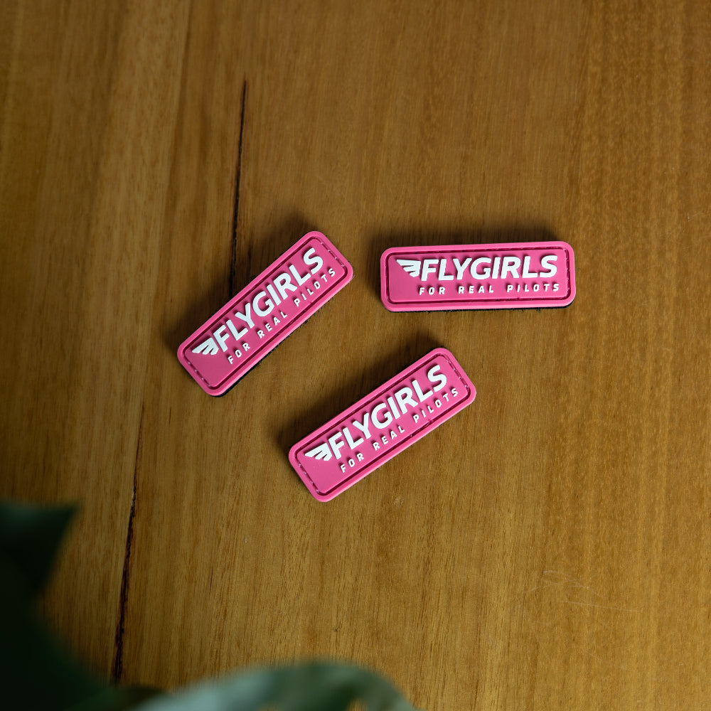 Three pink 'FLYGIRLS' patches on a wooden surface