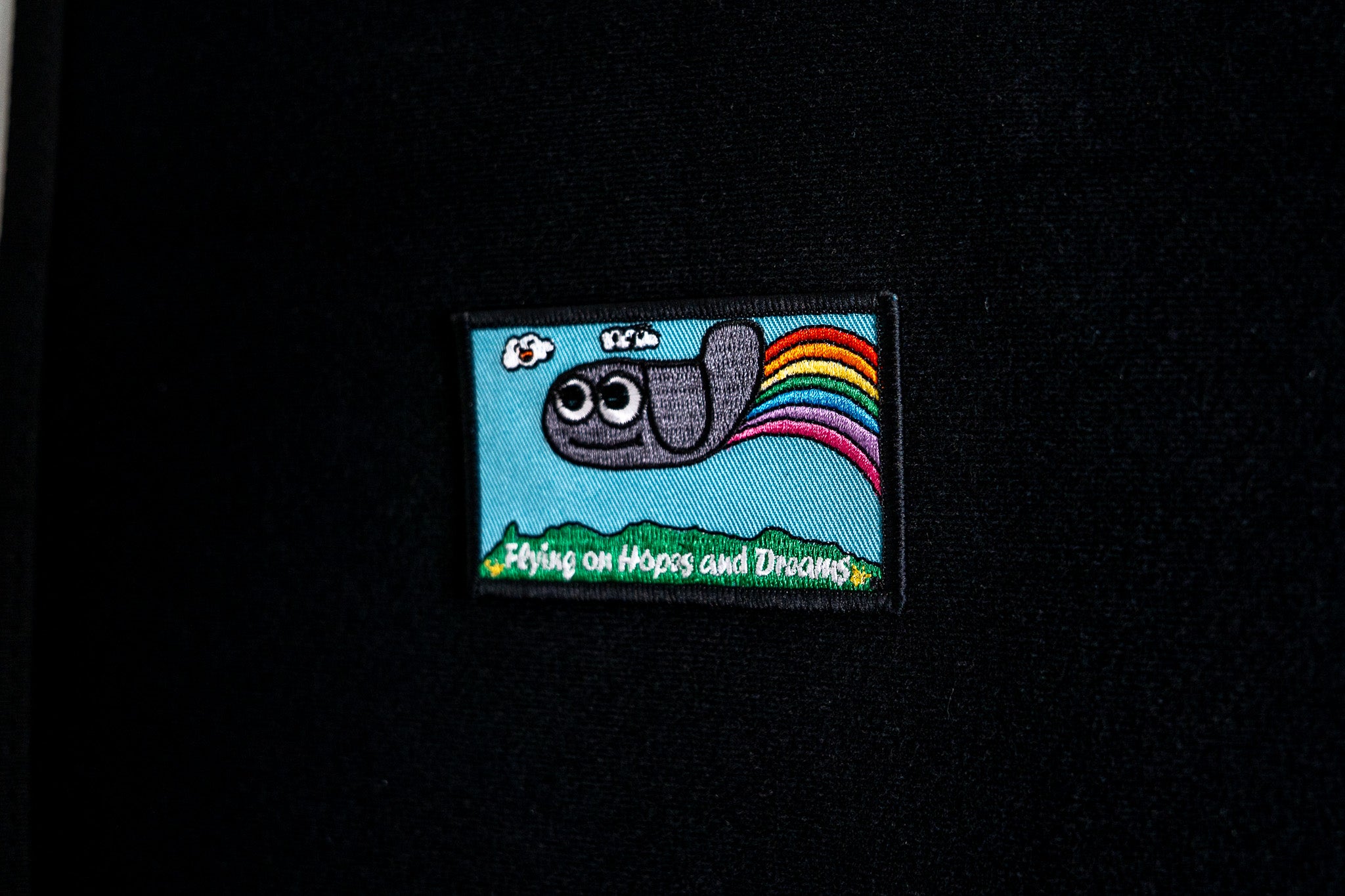 Embroidered patch with a cartoon character and rainbow on a black background