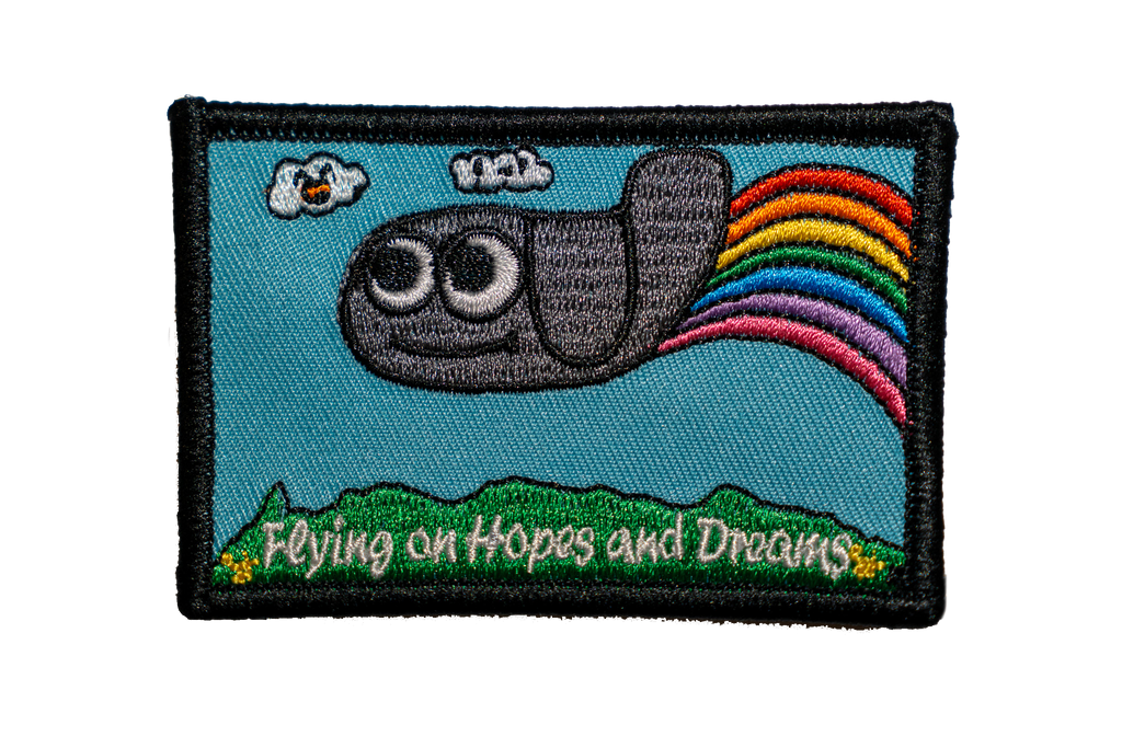 Embroidered patch with a cartoon plane, with a rainbow, and text 'Flying on Hopes and Dreams' on a blue background.