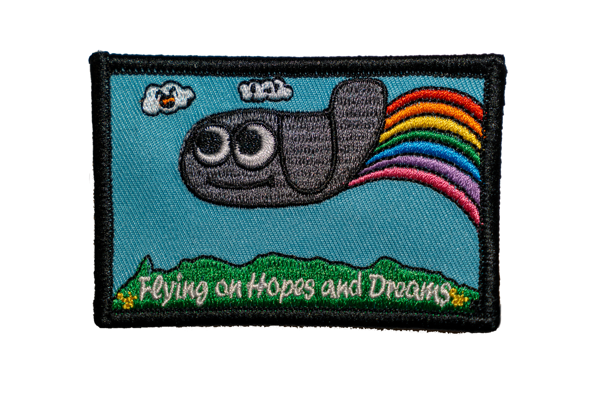 Embroidered patch with a cartoon plane, with a rainbow, and text 'Flying on Hopes and Dreams' on a blue background.